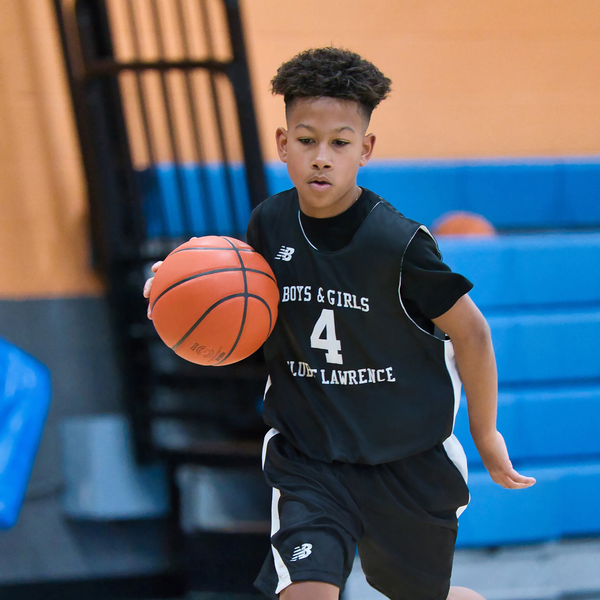 A medium - dark skinned male - presenting pre - teen dribbling a basketball.