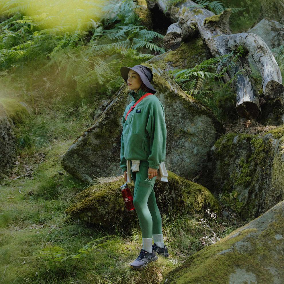 A person wearing New Balance apparel and trail shoes standing in a forest looking pensive. 