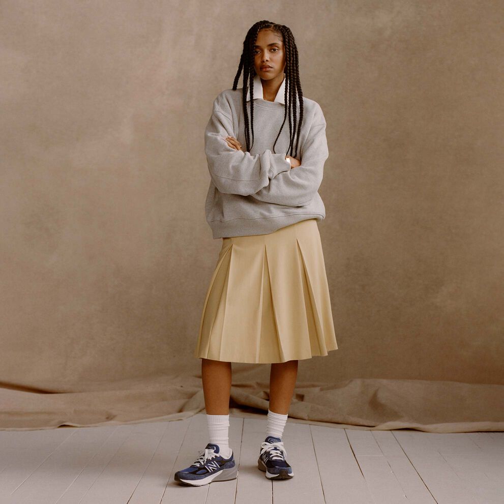  woman wearing blue Made in USA 990v6 shoes in front of a tan studio backdrop.