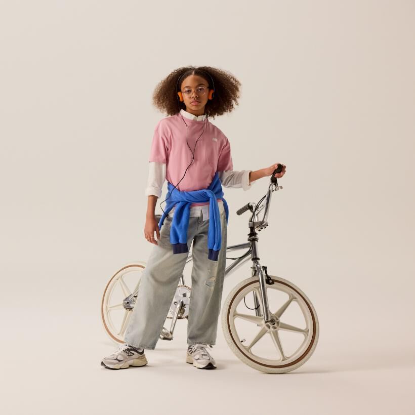 Young girl posing in front of a bike wearing New Balance 9060 sneakers 