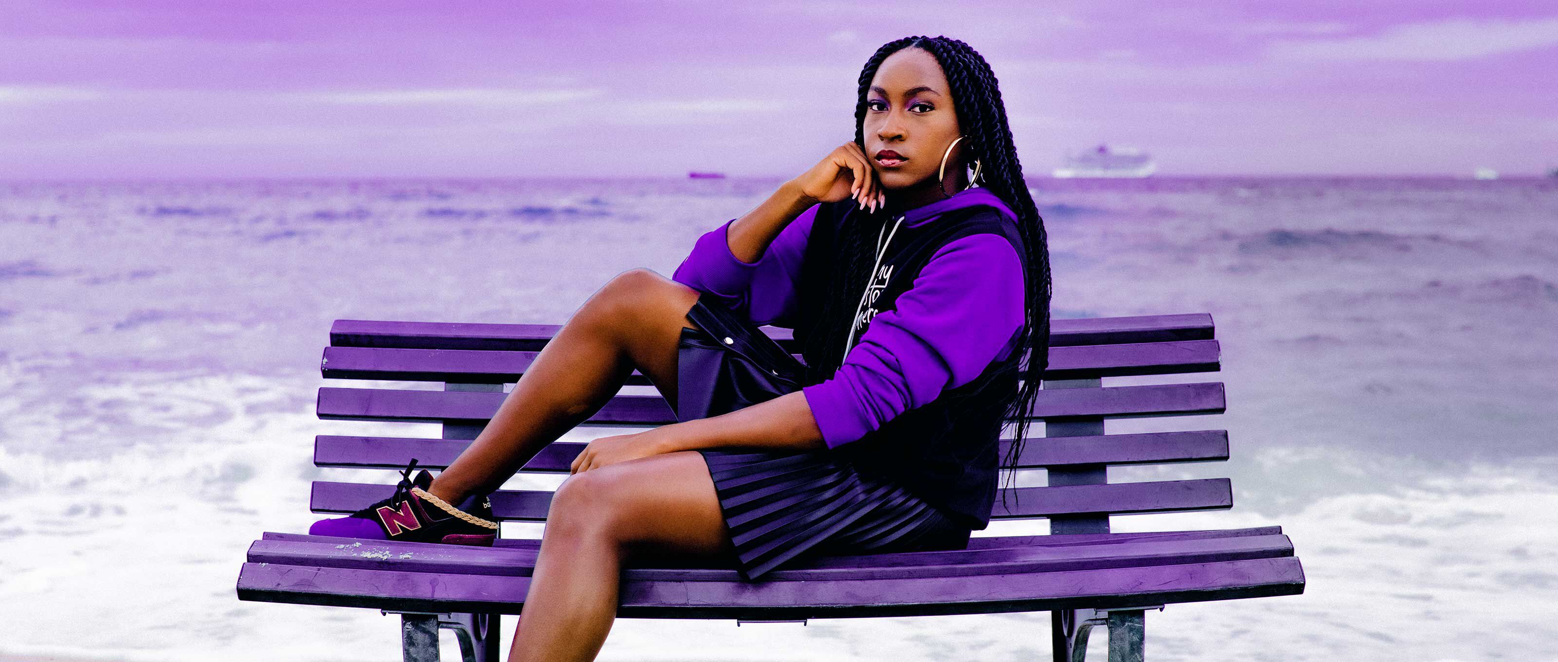Coco Gauff sitting on a park bench by the ocean wearing New Balance shoes and apparel