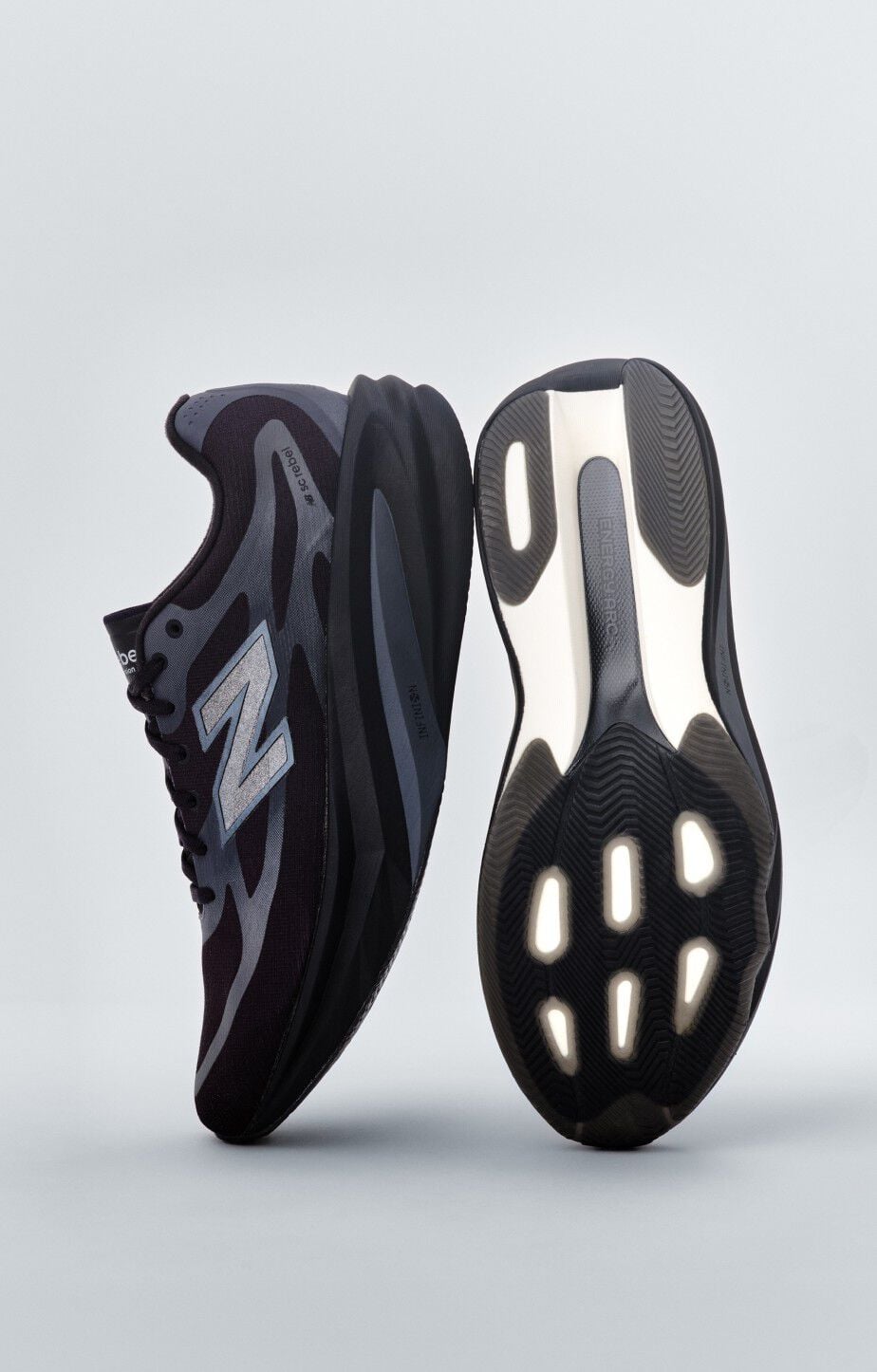 A pair of black New Balance sneakers sitting on a gray studio backdrop. 