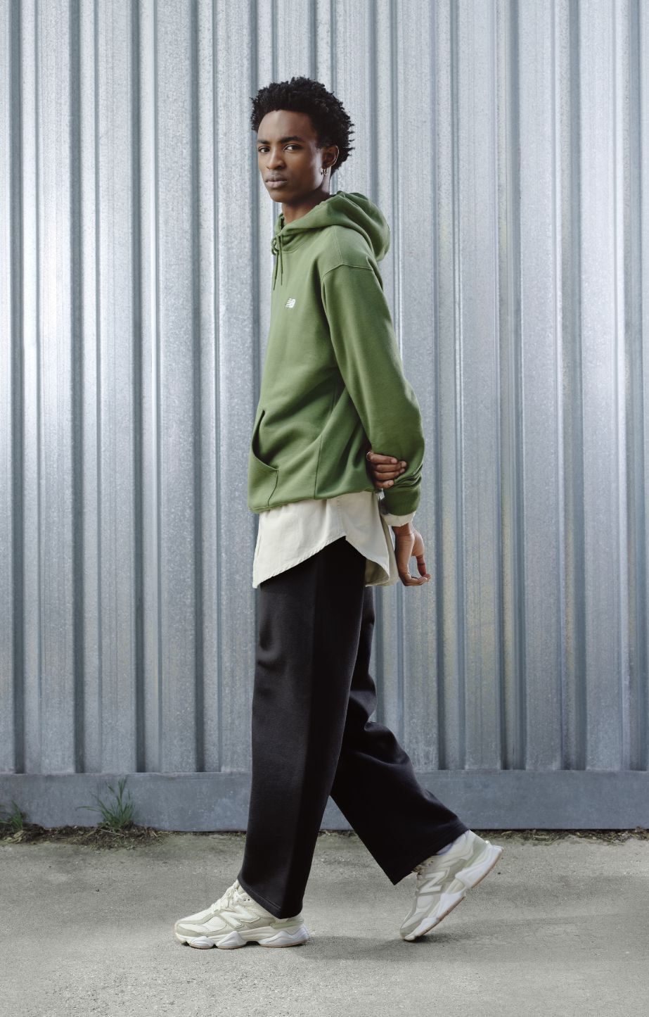 Man standing against a metal backgrop, wearing new balance 9060 sneakers