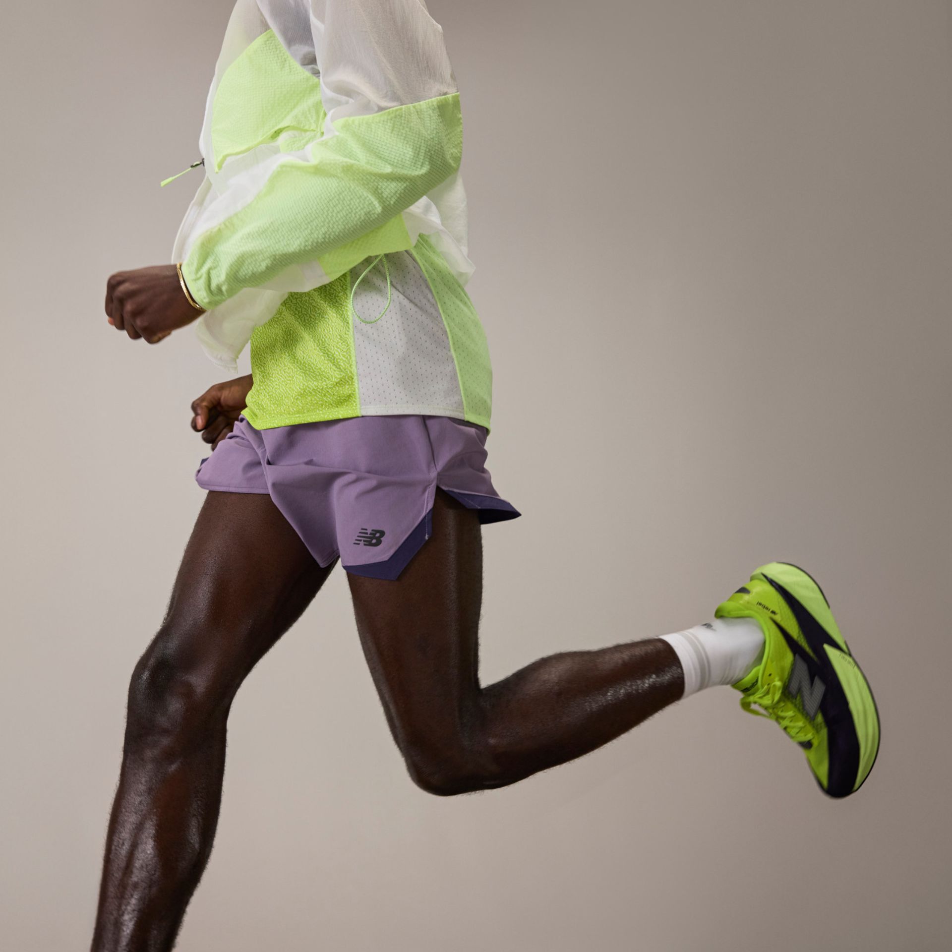 A man running in a pair of green and black FuelCell Rebel v5 shoes.