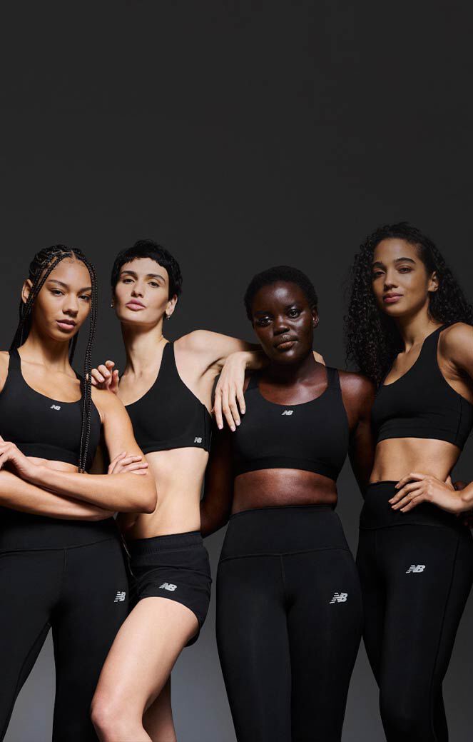 A group of women wearing sports bras and leggings in front of a black background. 