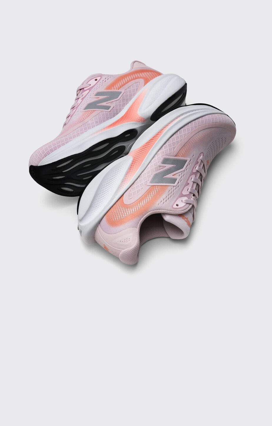 Pair of light pink New Balance running shoes with coral accents and chunky black-and-white soles displayed on a light gray background.