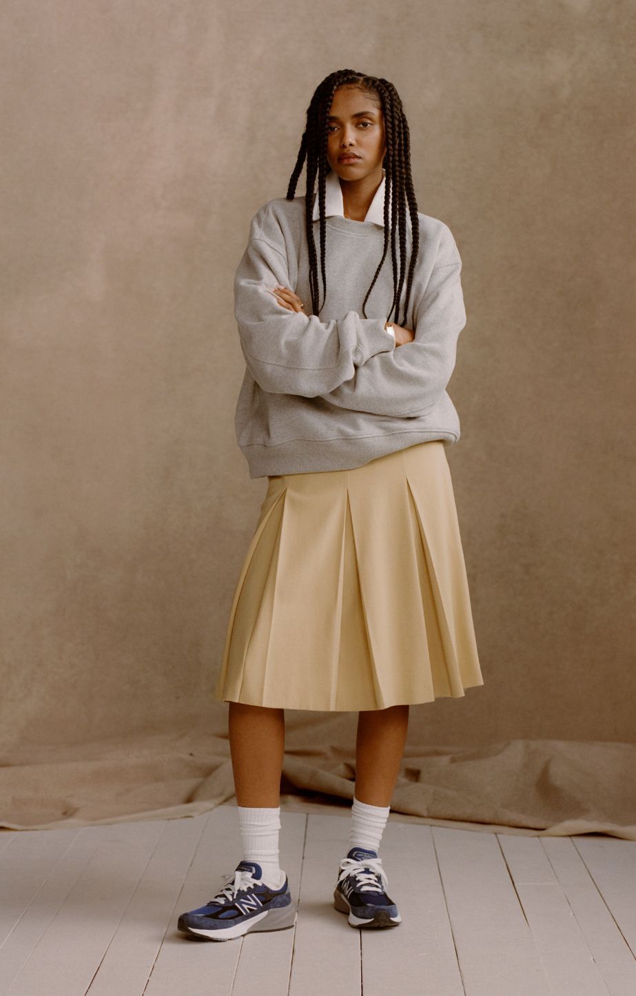  A woman wearing blue Made in USA 990v6 shoes in front of a tan studio backdrop.