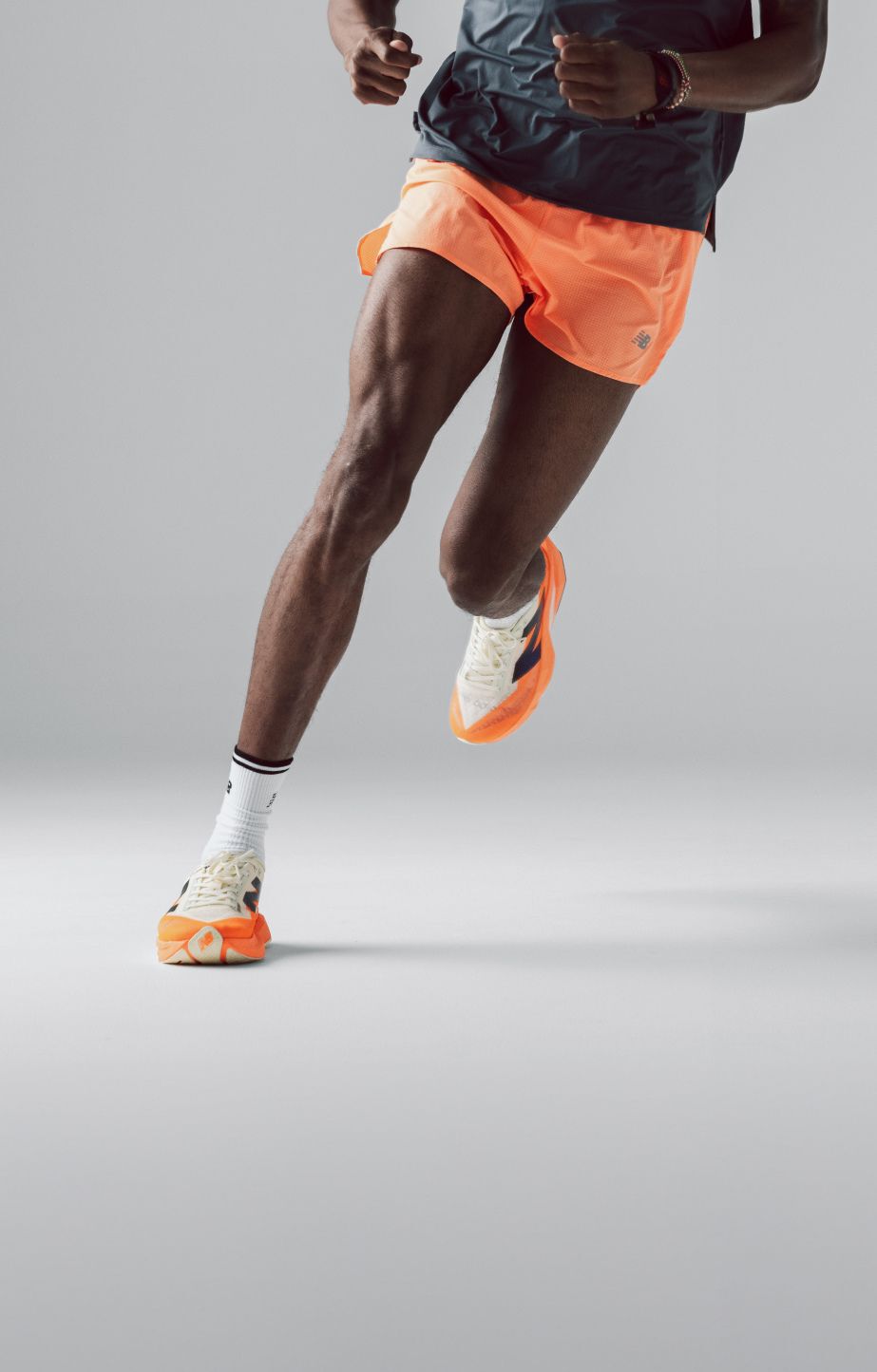 Young man in bright orange shorts running on a grey background. 