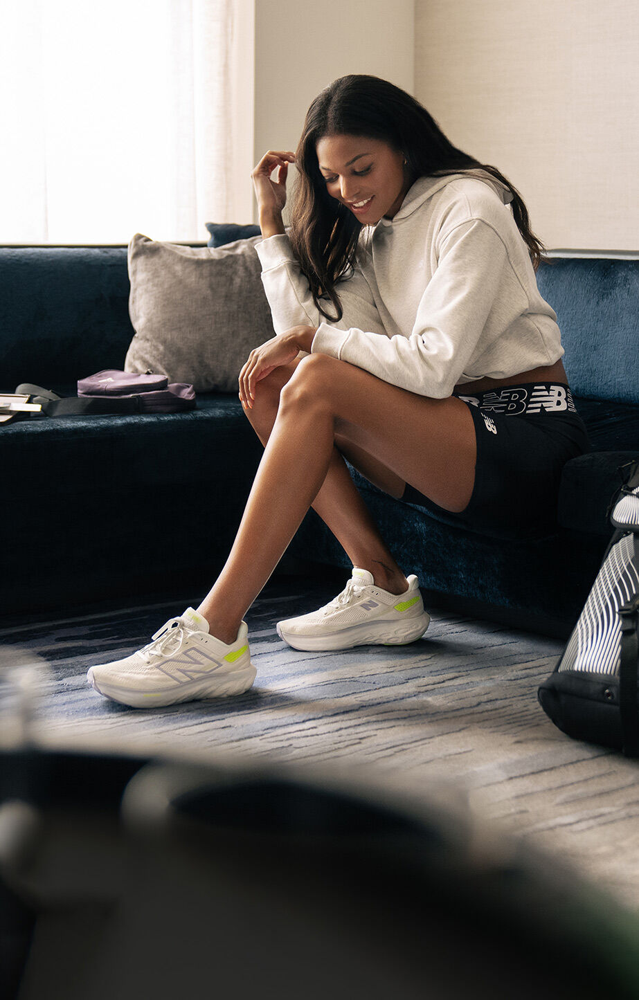 Gabby Thomas sitting in a hotel room wearing white and green Fresh Foam X 1080 shoes. 