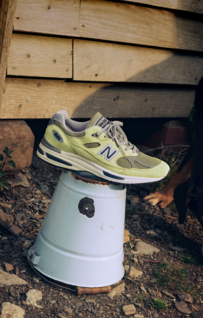 A pair of New Balance Made in UK sneakers on a raw earth surface of dirt and stones. 