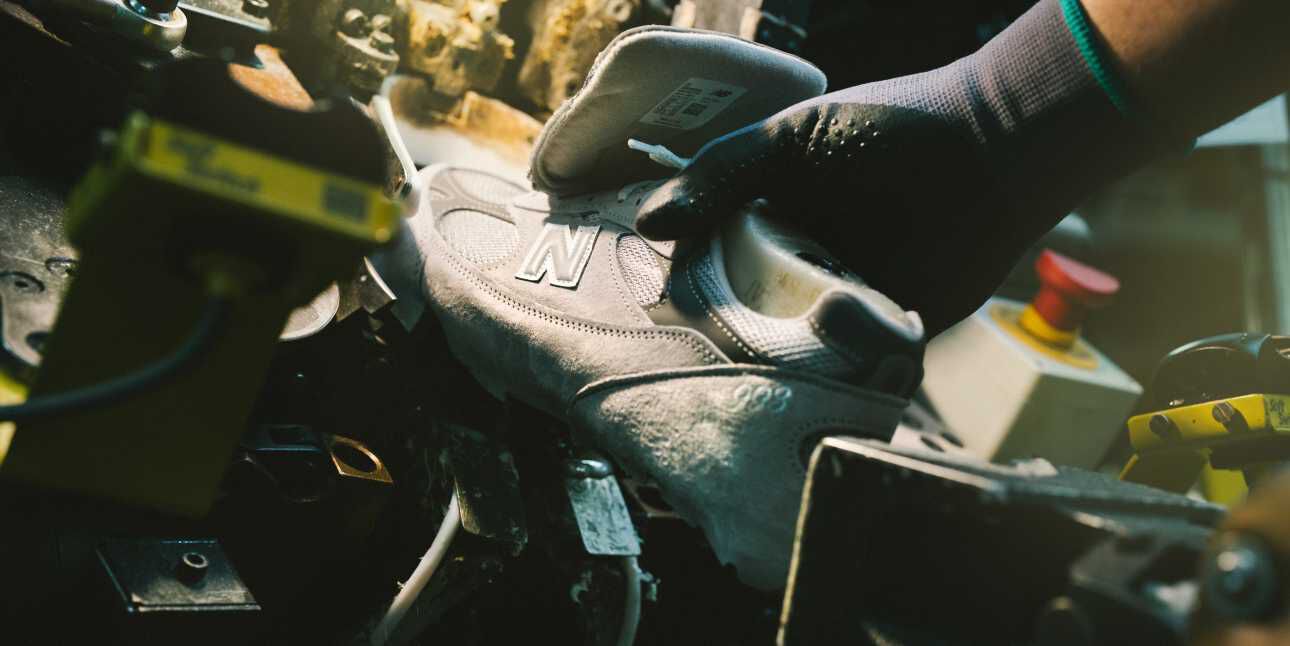 A New Balance sneaker sitting in equipment and being constructed in a factory setting. 