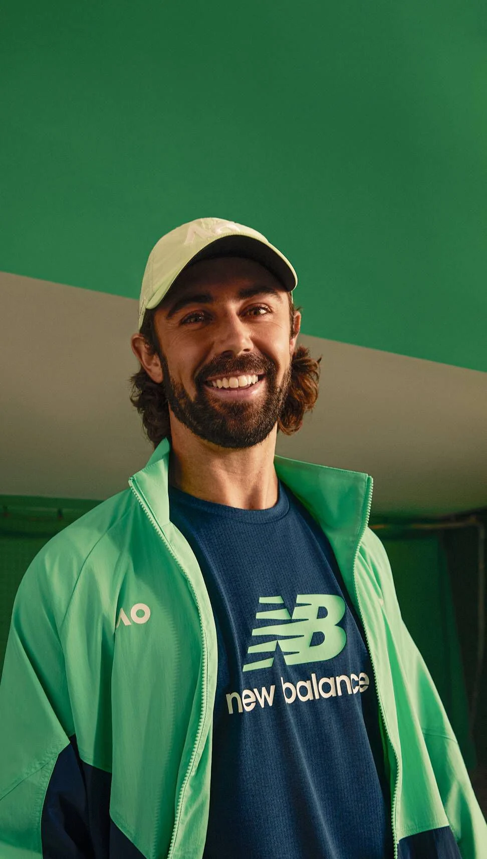 A man looking at the viewer and smiling while wearing New Balance clothing.