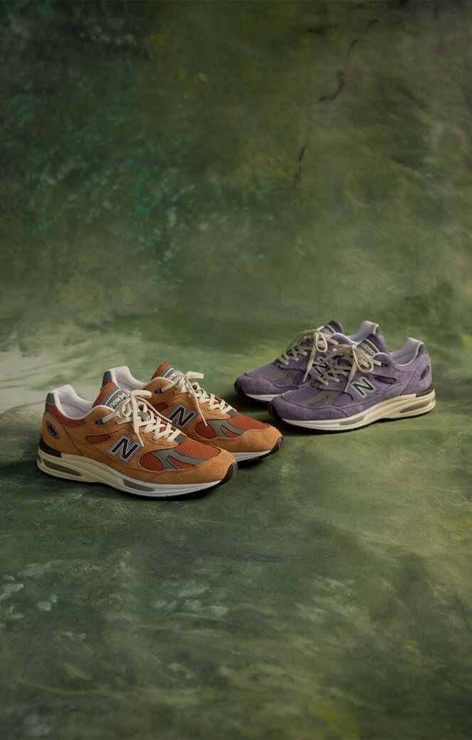 Two pairs of New Balance Made in UK sneakers in a green textured studio environment.